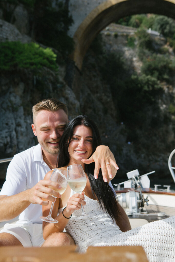 Newly engaged couple sitting on a boat having Prosecco toast after proposal
