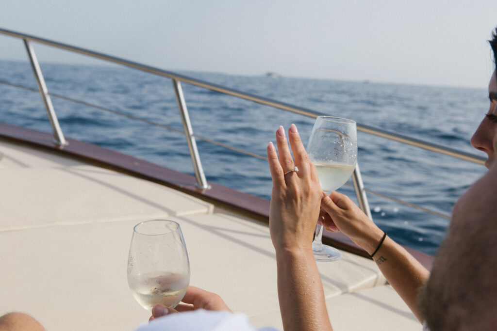 Woman showing off her engagement ring on a boat with Amalfi cliffs behind