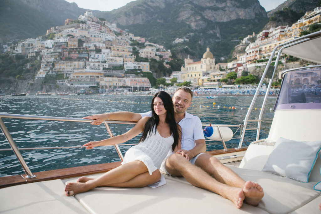 Couple posing on boat with Positano behind them after surprise engagement