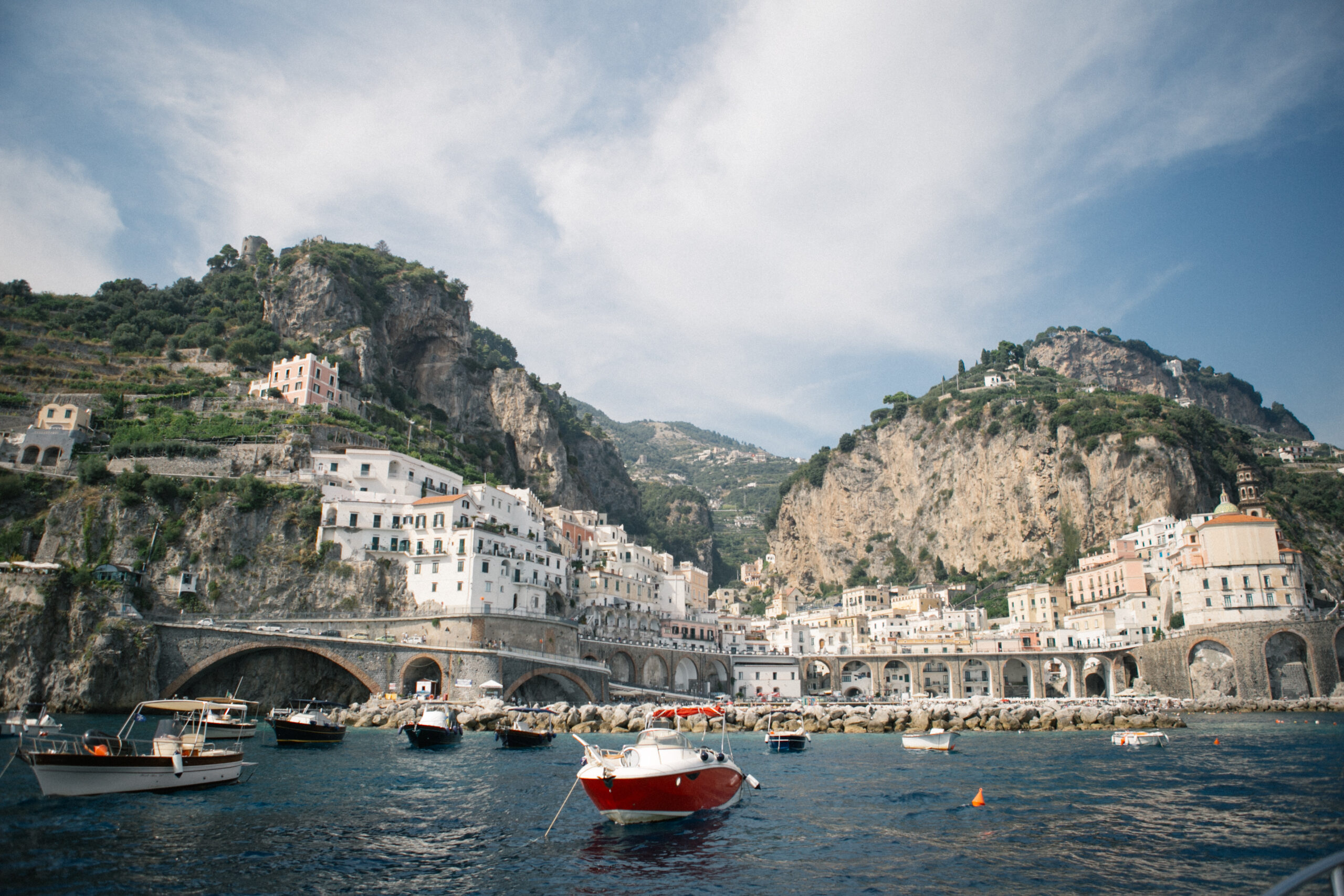Red boat anchored in the turquoise waters of the Amalfi Coast with pastel cliffside buildings in the background — a dreamy and romantic setting for an intimate Italian elopement