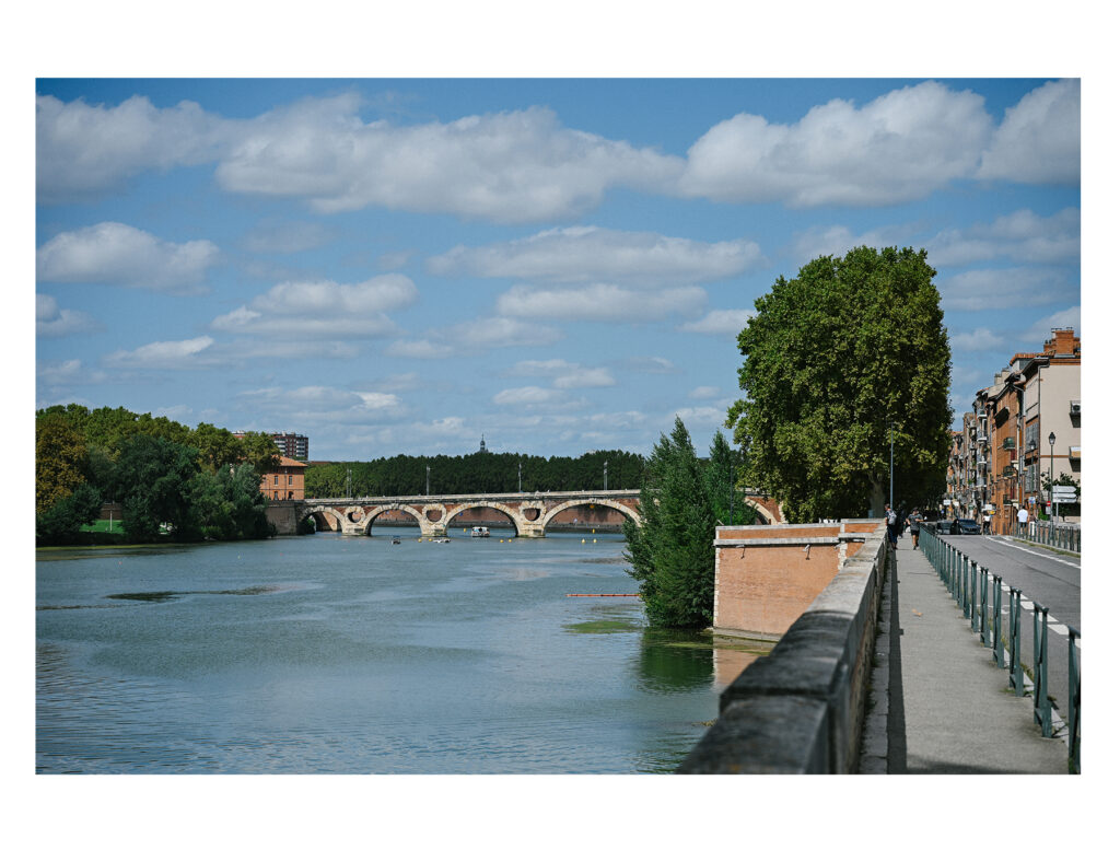 Toulouse riverbank with stone bridge at golden hour.