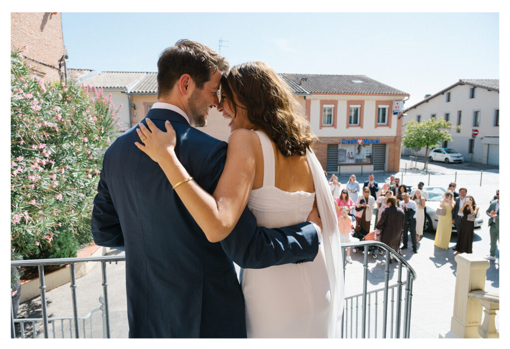 Bride and groom embrace on church steps as guests cheer after Toulouse wedding ceremony.