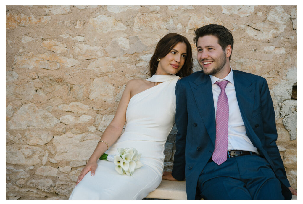 Bride and groom sitting against rustic stone wall at Le Manoir de Lisle, captured by Toulouse wedding photographer.
