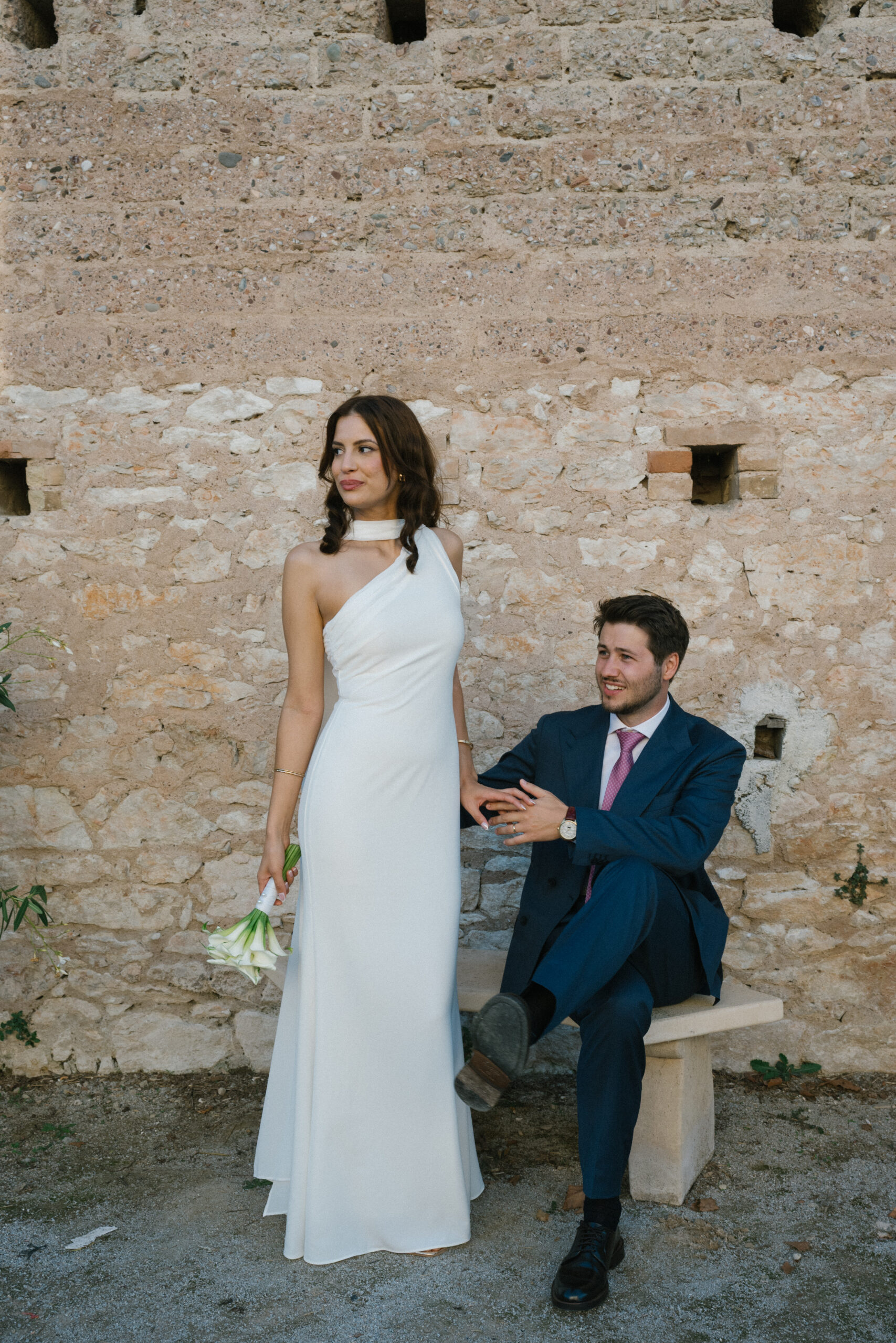 Bride and groom sitting against rustic stone wall at Le Manoir de Lisle, captured by Toulouse wedding photographer.