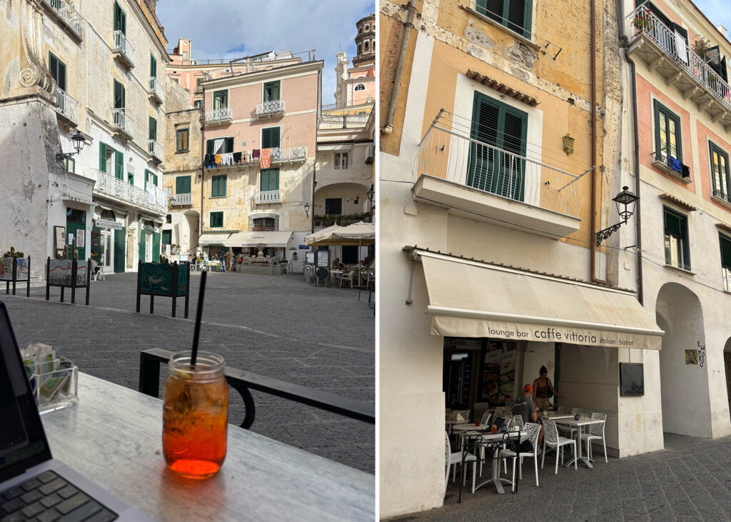 Working from a café in Atrani piazza with a laptop and Aperol spritz, surrounded by pastel buildings on the Amalfi Coast.
