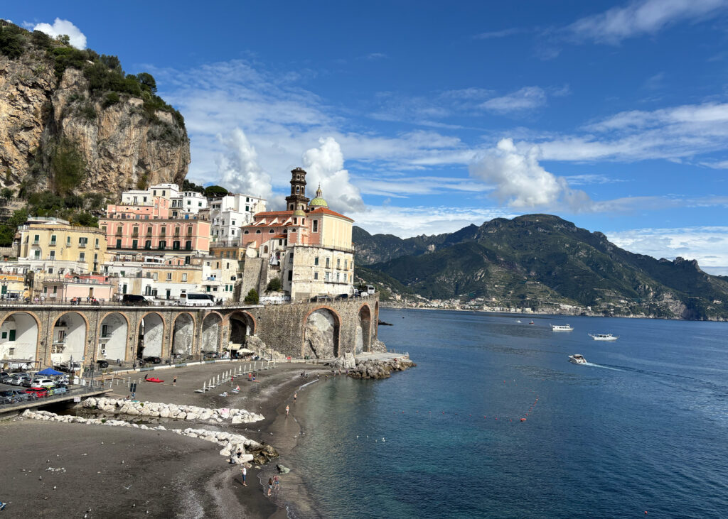View of Atrani village on the Amalfi Coast — pastel buildings, cliffside arches, and the Tyrrhenian Sea under a blue sky. Atrani Amalfi Coast travel guide.